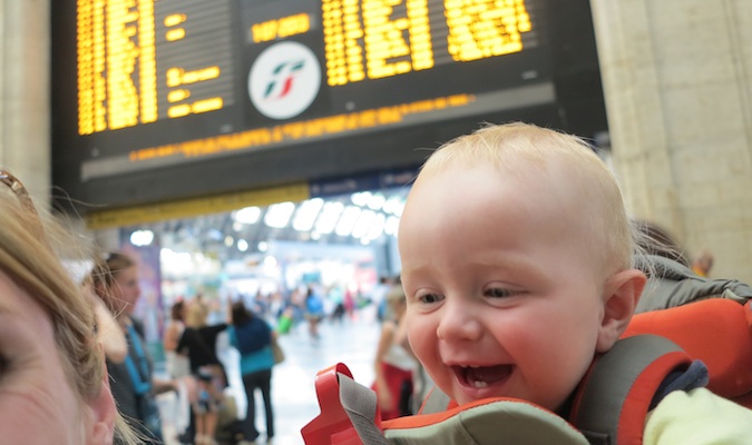 son in a baby carrier posing at a train station in Europe