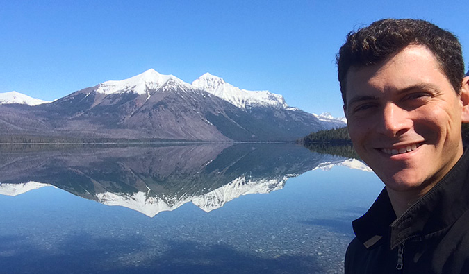 Matt Kepnes standing in front of some mountains while traveling, with a big blue sky above