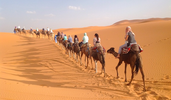 Nomadic Matt taking a camel ride through the Sahara desert in Morocco with a group of other travelers