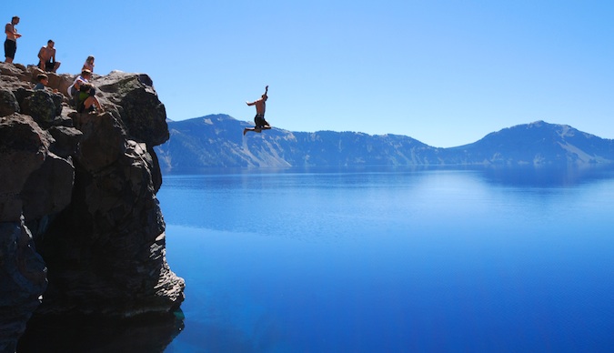 An adventurous traveler leaping for a cliff into inviting blue water