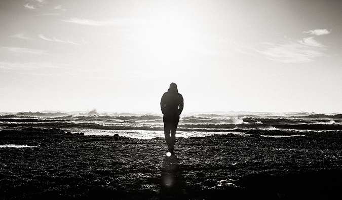 A black and white photo of a man walking alone on a beach