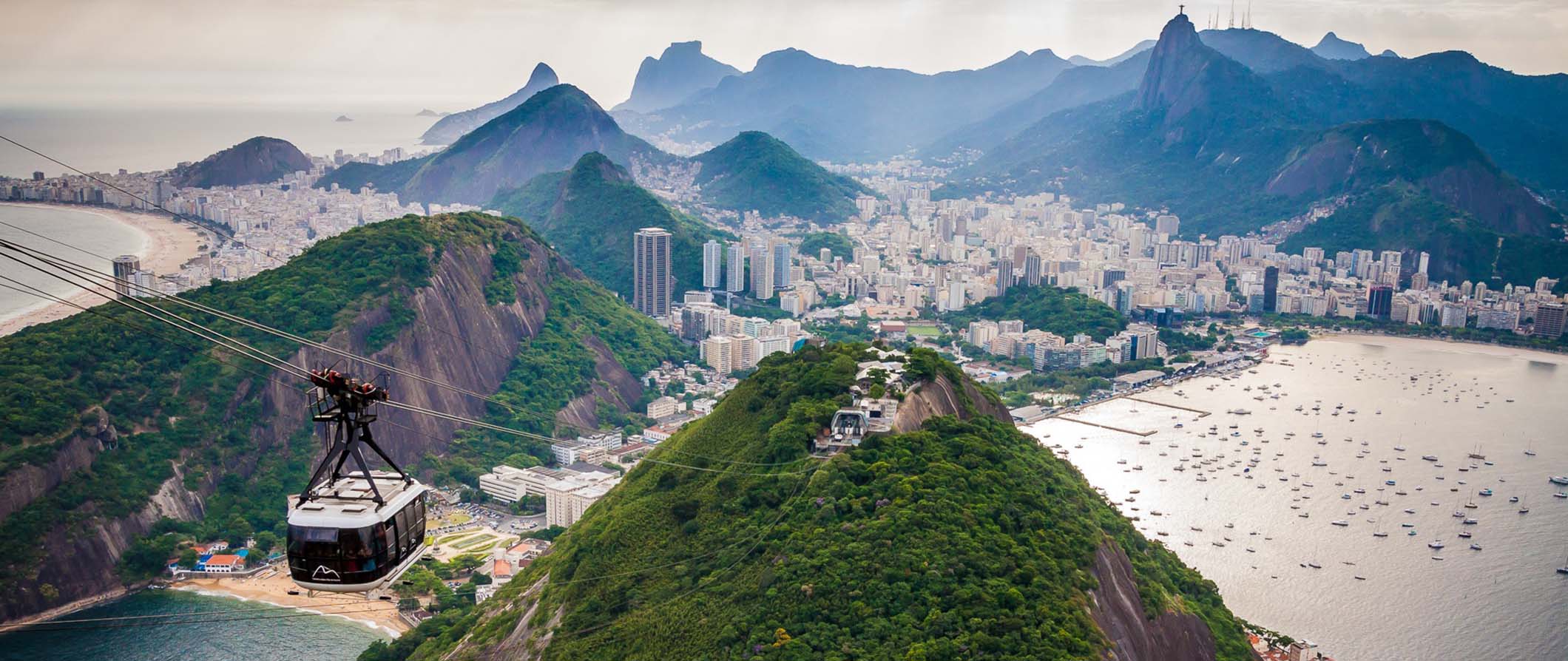 The view of Rio de Janeiro from Sugarloaf Mountain with green mountains in the background and a cable car in the foreground