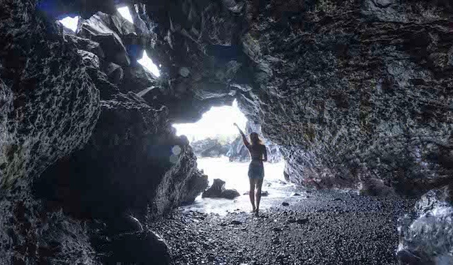 Solo female traveler posing for a photo in a cave near the ocean