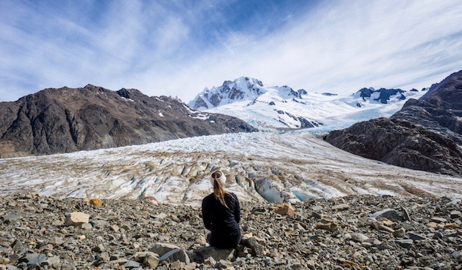 A solo female traveler sitting near snow-covered mountains