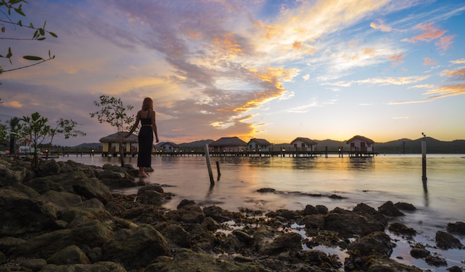 A solo female traveler in front of incredible sunrise near water bungalows in Asia