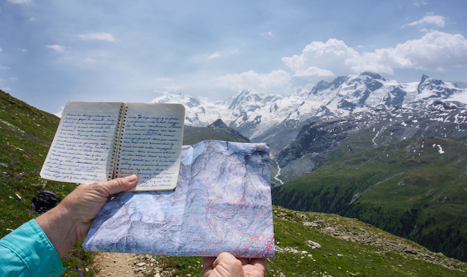 Travel journal held up in front of an amazing snow-capped mountain range overseas