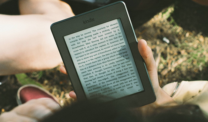 A traveler sitting in the grass reading a Kindle e-reader