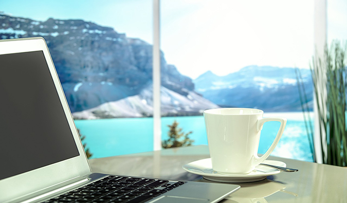 A photo of a up of coffee and a laptop near a window with a scenic view