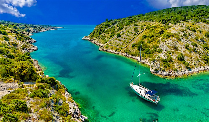 a sailboat floating up a narrow river with beautiful turquoise water