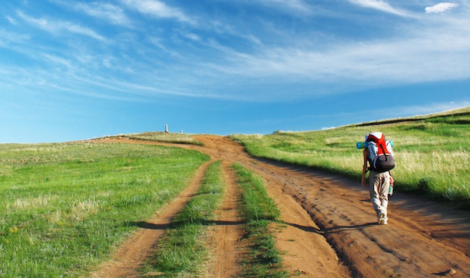 A nomadic backpacker hiking in a field surrounded by grass