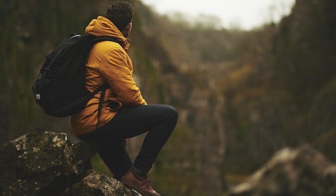 A solo hiker in a yellow jacket sitting in the mountains looking at the scenery around him