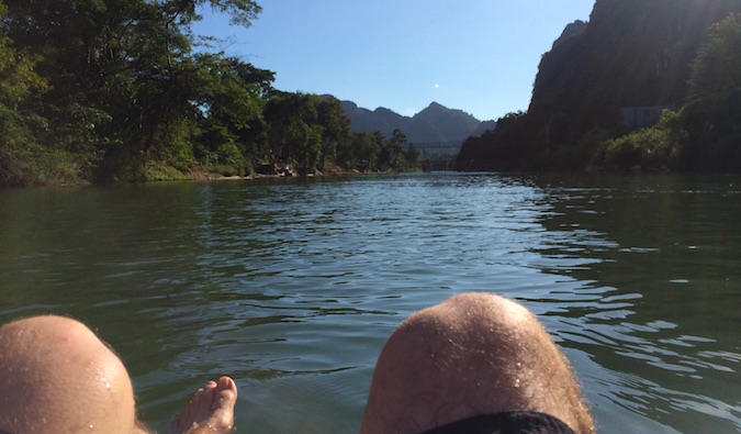 A man's legs point of view from a river raft in Vang Vieng, Laos
