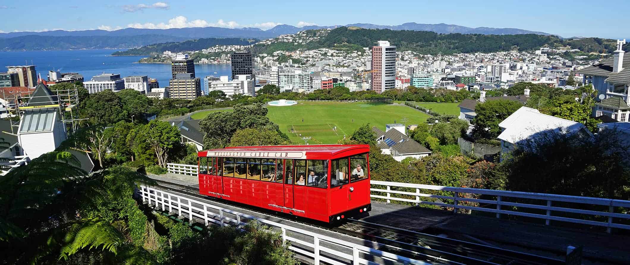 The red Wellington cable car going up the hillside with the city of Wellington, New Zealand in the background.